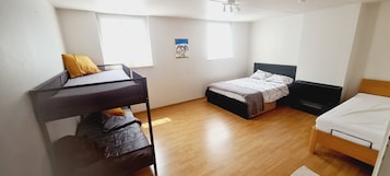 Una habitación con literas, una cama individual y un escritorio. Dos ventanas dejan entrar luz natural.
