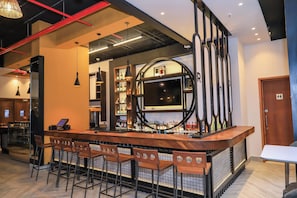 Un espace bar doté d’un long comptoir, de nombreux tabourets et d’étagères remplies de bouteilles.