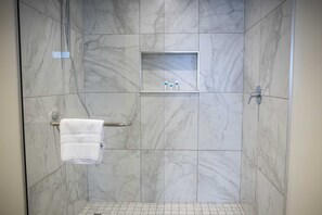 Eine Dusche mit Marmorwänden, einem Handtuchhalter und einem Ablagefach für Toilettenartikel.