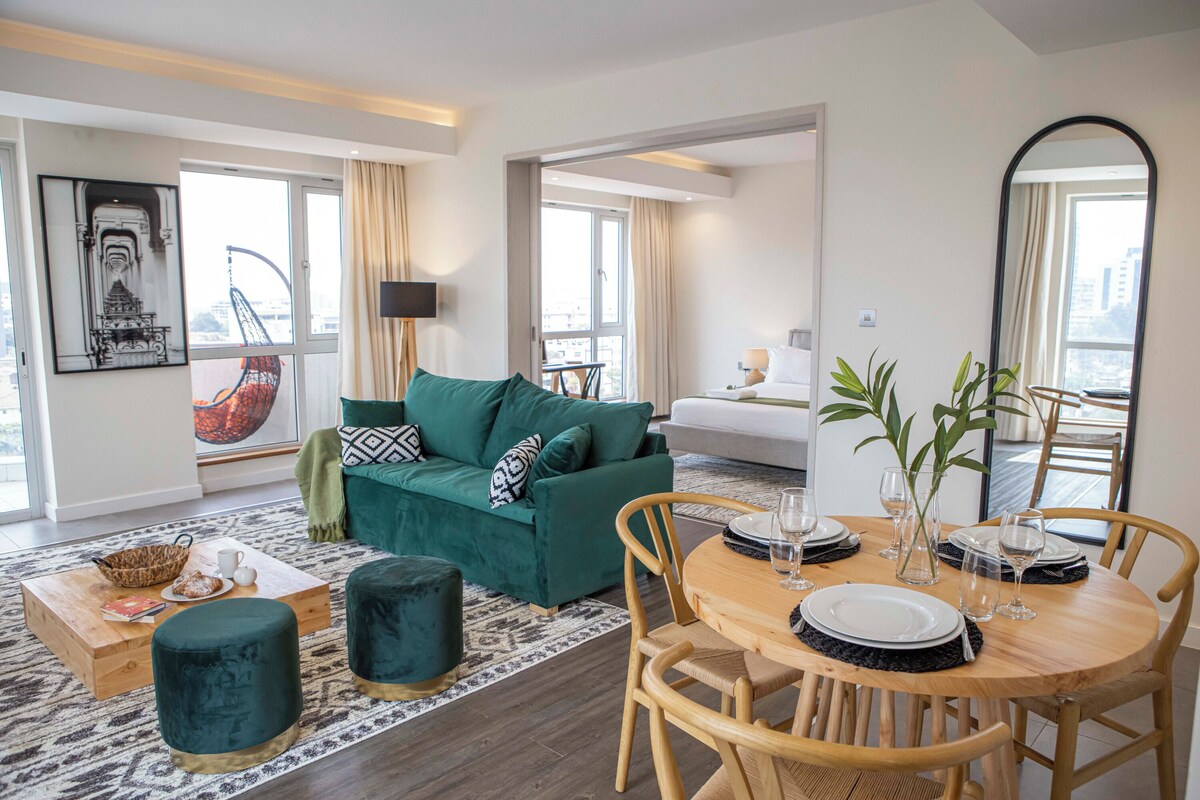 Un salon moderne avec un canapé vert, une table basse en bois et un coin repas comprenant une table et des chaises en bois.