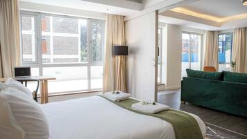 A hotel room with a large bed, a desk with a laptop, a green sofa, and a TV.