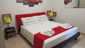 A neatly arranged hotel room with a bed, pillows, a red headboard, a nightstand with a lamp, and a wall with a car-themed artwork. - Il Cavallino vacation home on Lake Ceresio and Lugano (Lombardia)