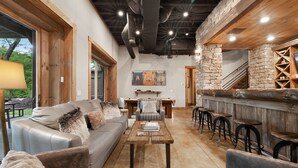 A cozy living area with a sofa, coffee table, and bar stools. There is a staircase leading to an upper level. - On Toccoa River - Luxury Riverfront - Hot tub (Mineral Bluff)