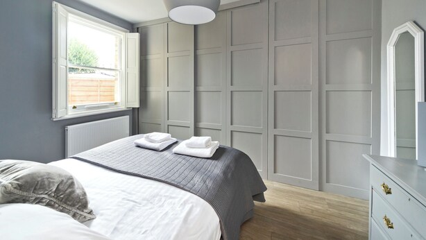 A bedroom with a bed, a dresser, a radiator, a window, and a wall paneling. - Twickenham Green (Twickenham)