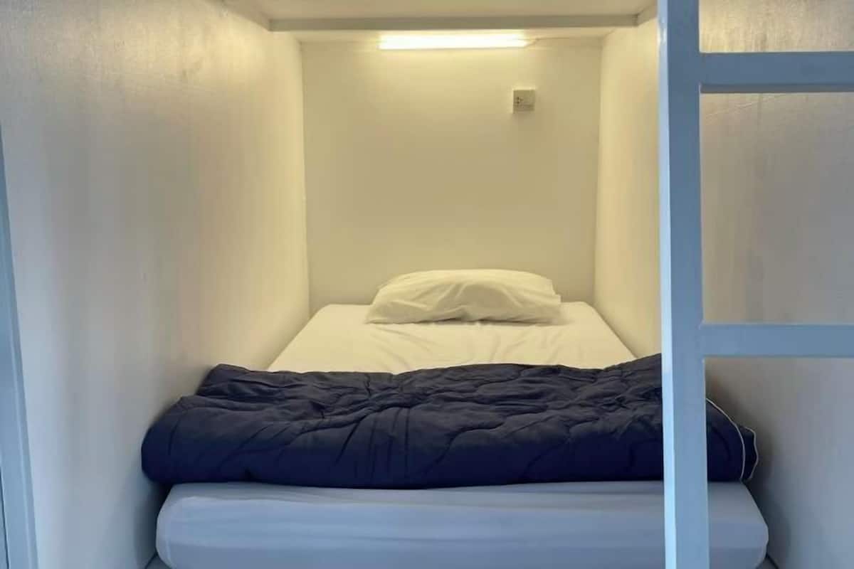 A small, single-bed room with a white headboard, a black bedspread, and a white pillow.
