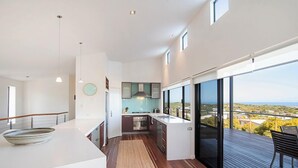A modern kitchen with a large island, a dining area with a view, and a balcony with a wooden deck.