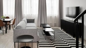 A modern living room with a sofa, a dining table with chairs, a black and white rug, a TV, and a staircase.
