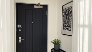 A black door with a keyhole and a lock, a potted plant on a black console table, and a framed artwork on the wall. - OneFiveSix Unique ApartHotel 2-Bed 2-Bathroom (Birmingham)