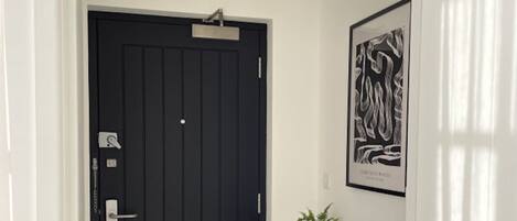 A black door with a keyhole and a lock, a potted plant on a black console table, and a framed artwork on the wall.