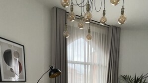 A round wooden dining table with six chairs, a potted plant, a floor lamp, and a framed picture on the wall. - OneFiveSix Unique ApartHotel 2 Bed (West Midlands)