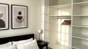 A bedroom with a bed, a nightstand, a lamp, and a wardrobe with shelves. - OneFiveSix Unique ApartHotel 2 Bed (West Midlands)