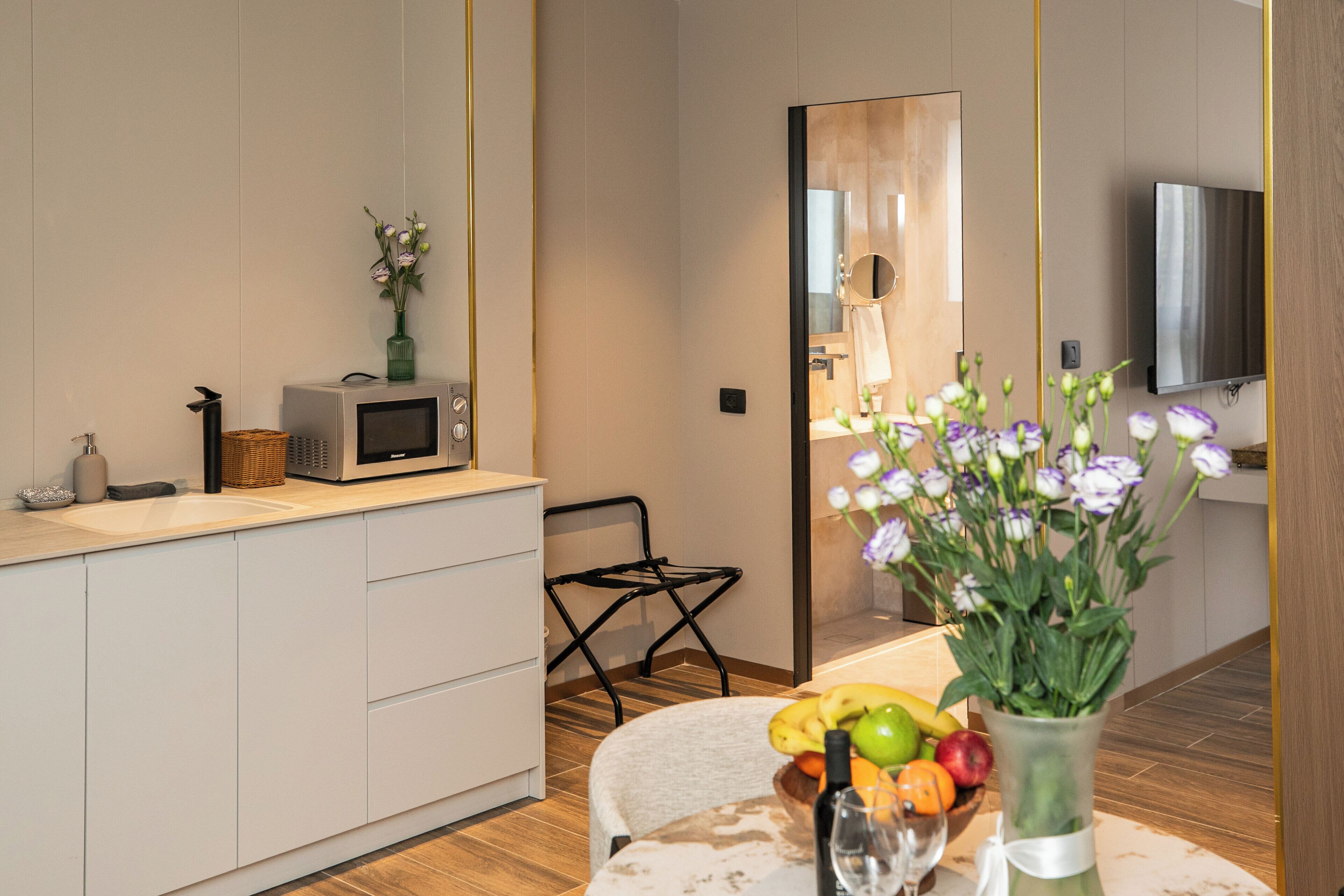 A modern kitchen with white cabinets, a microwave, a wicker basket, and a dining area with a table set for two.