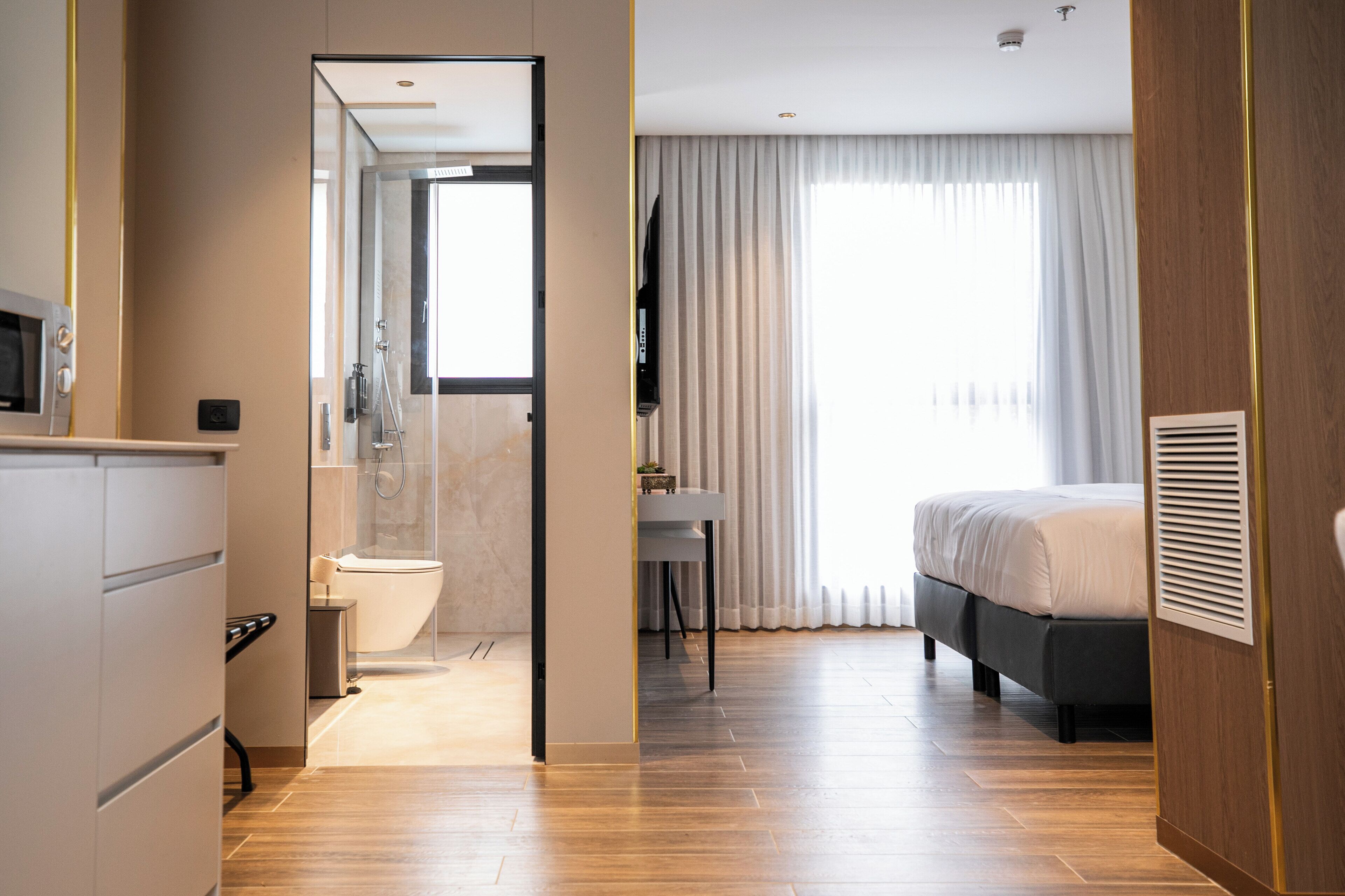 Une chambre d’hôtel moderne avec un plancher en bois, un lit, un bureau et une salle de bain équipée d’une douche et de toilettes.