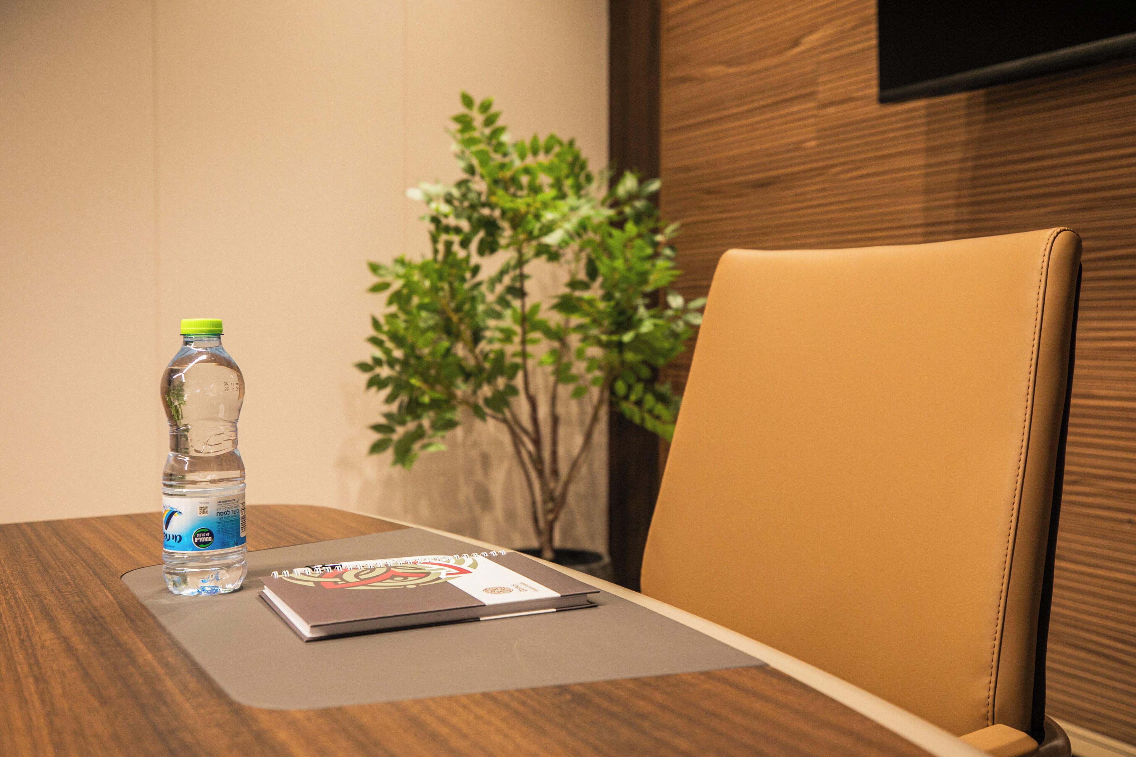 A conference room with a wooden table, a laptop, a water bottle, and a potted plant.