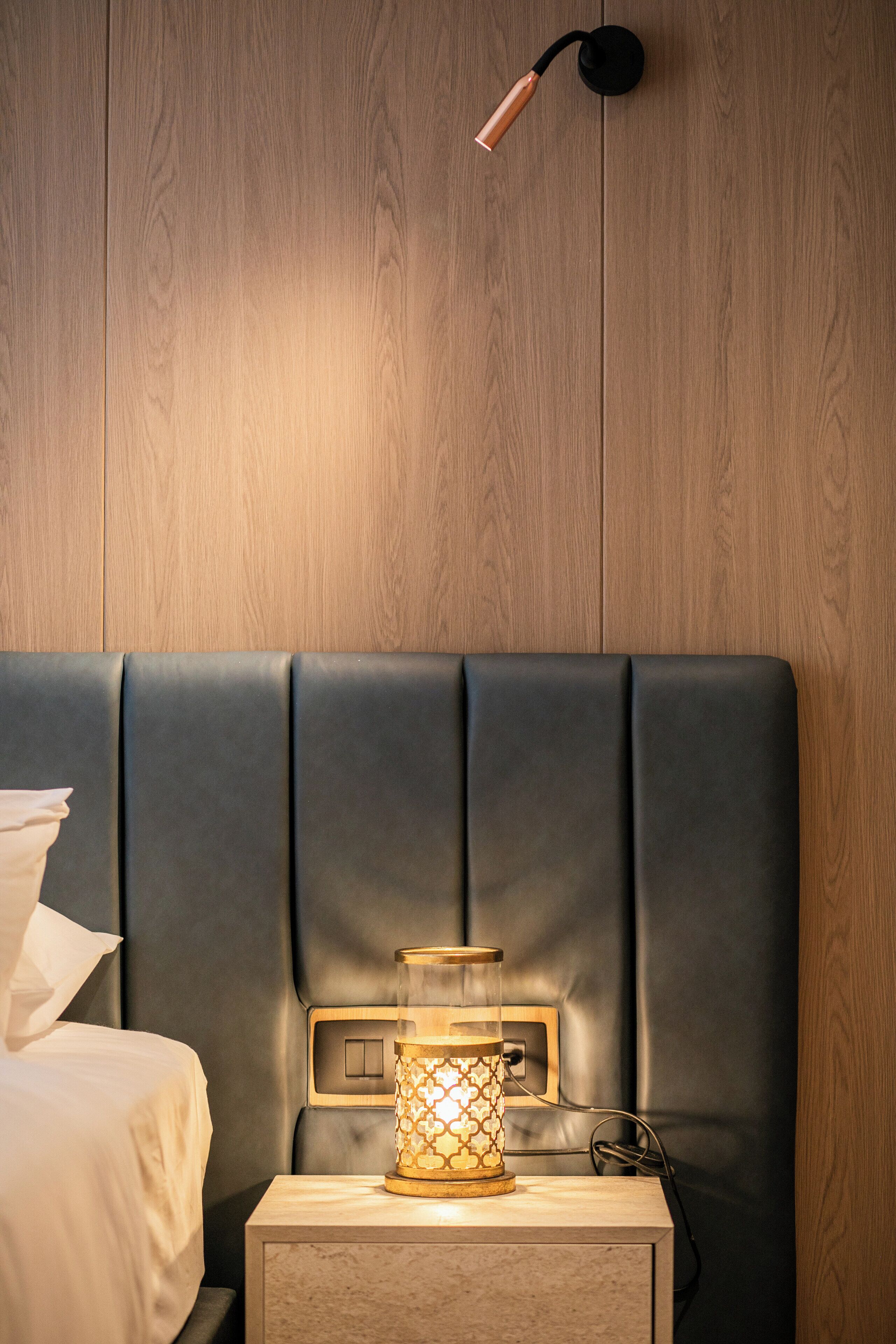 Un lit avec une tête de lit, une table de chevet avec une lampe et un mur recouvert de lambris en bois.