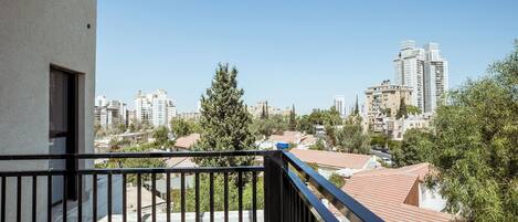 A balcony with a view of a cityscape, including residential buildings and a tall skyscraper.