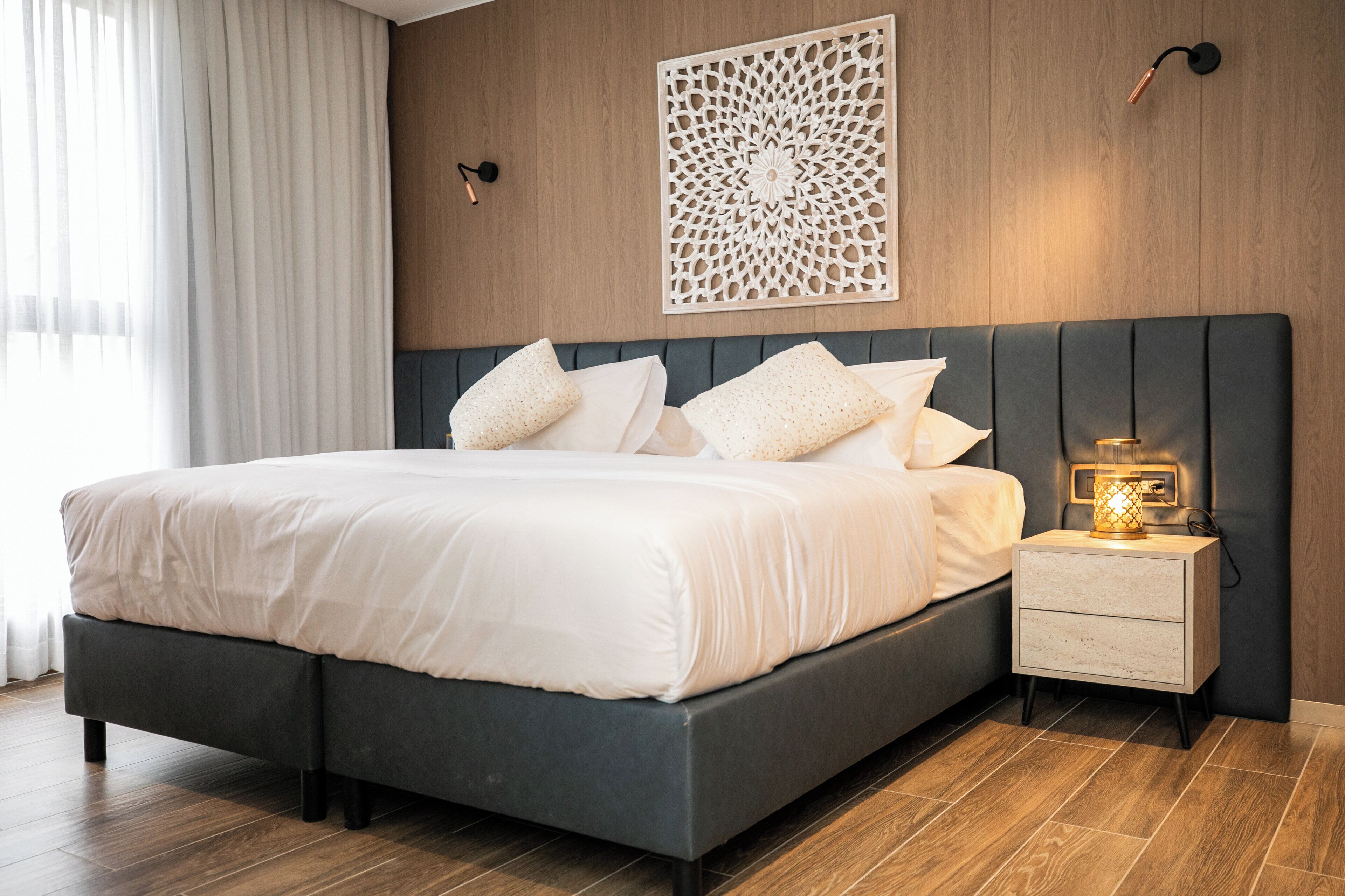 Un dormitorio moderno con una cama grande, una mesita de noche con lámpara y un elemento decorativo en la pared.