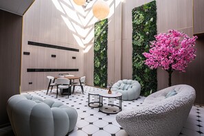 Un interior moderno con un patrón geométrico en el suelo, una mesa redonda con sillas y un gran árbol de flores rosadas.