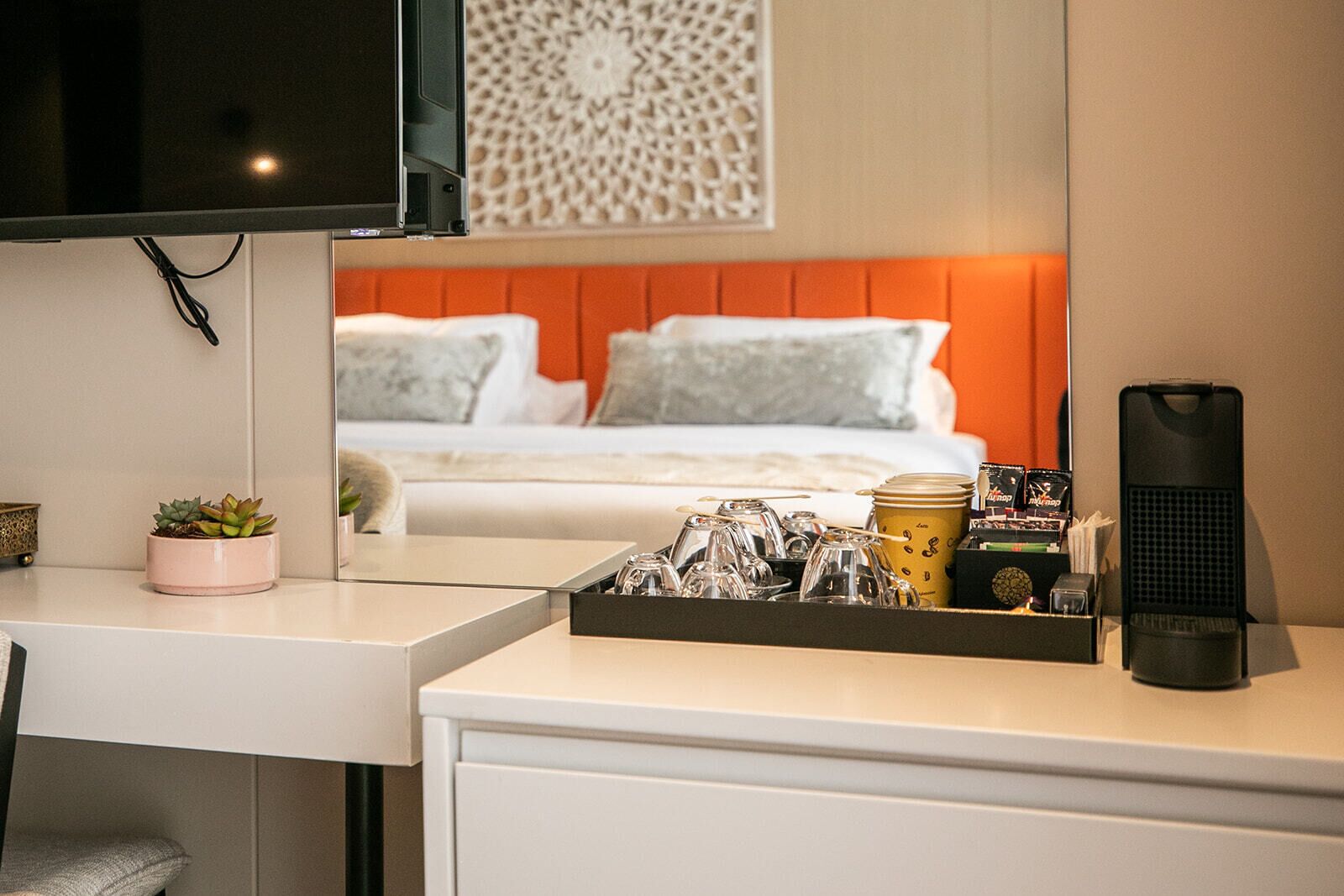 Quarto de hotel com uma cama, uma escrivaninha com um conjunto de objetos, uma televisão e um painel decorativo na parede.