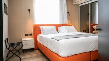 A modern hotel room with a large bed, a nightstand, a chair, and a wardrobe.