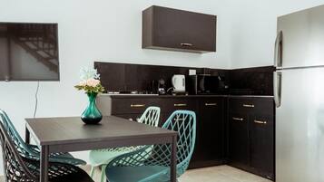 A modern kitchen with dark cabinetry, a stainless steel refrigerator, and a dining area with a wooden table and chairs.