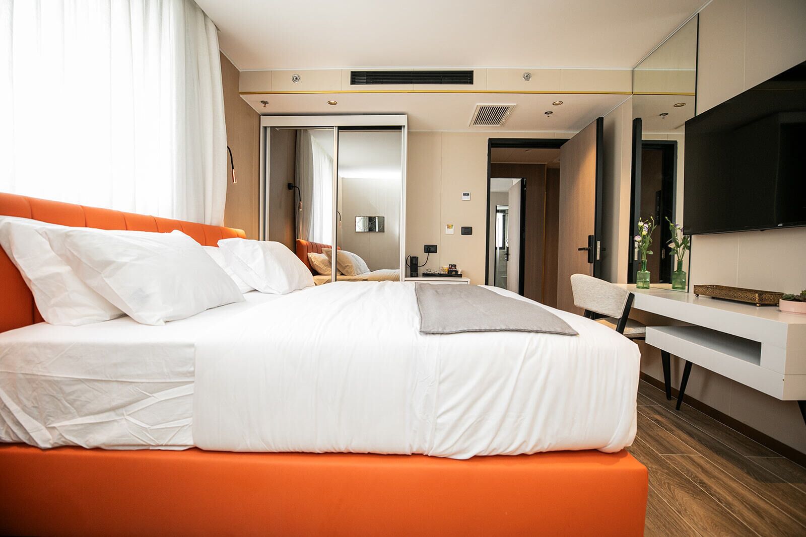 A modern hotel room with a large bed, a desk, a chair, and a TV.