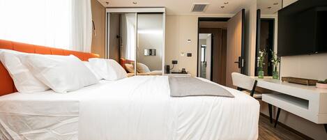 A modern hotel room with a large bed, a desk, a chair, and a TV.