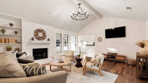 A spacious living room with a fireplace, a television mounted on the wall, and a chandelier. - Radiant & Refined | Stylish 4BR Home in Round Rock (Round Rock)