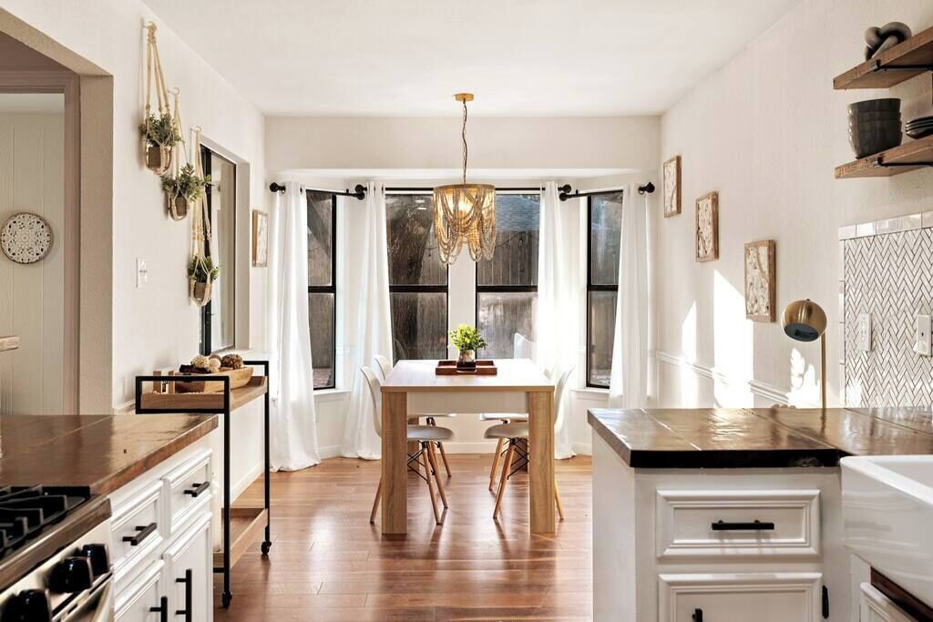 A modern kitchen with a wooden table, white cabinets, and a hanging light fixture.