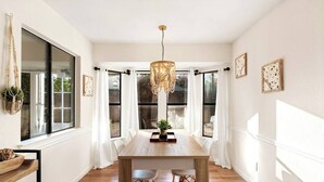 A dining area with a wooden table, white chairs, a chandelier, and large windows with white curtains. - Radiant & Refined | Stylish 4BR Home in Round Rock (Round Rock)