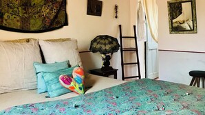 Ein Schlafzimmer mit einem Bett, einem Wandteppich, einer Leiter, einem Spiegel und einem kleinen Tisch mit einer Lampe.