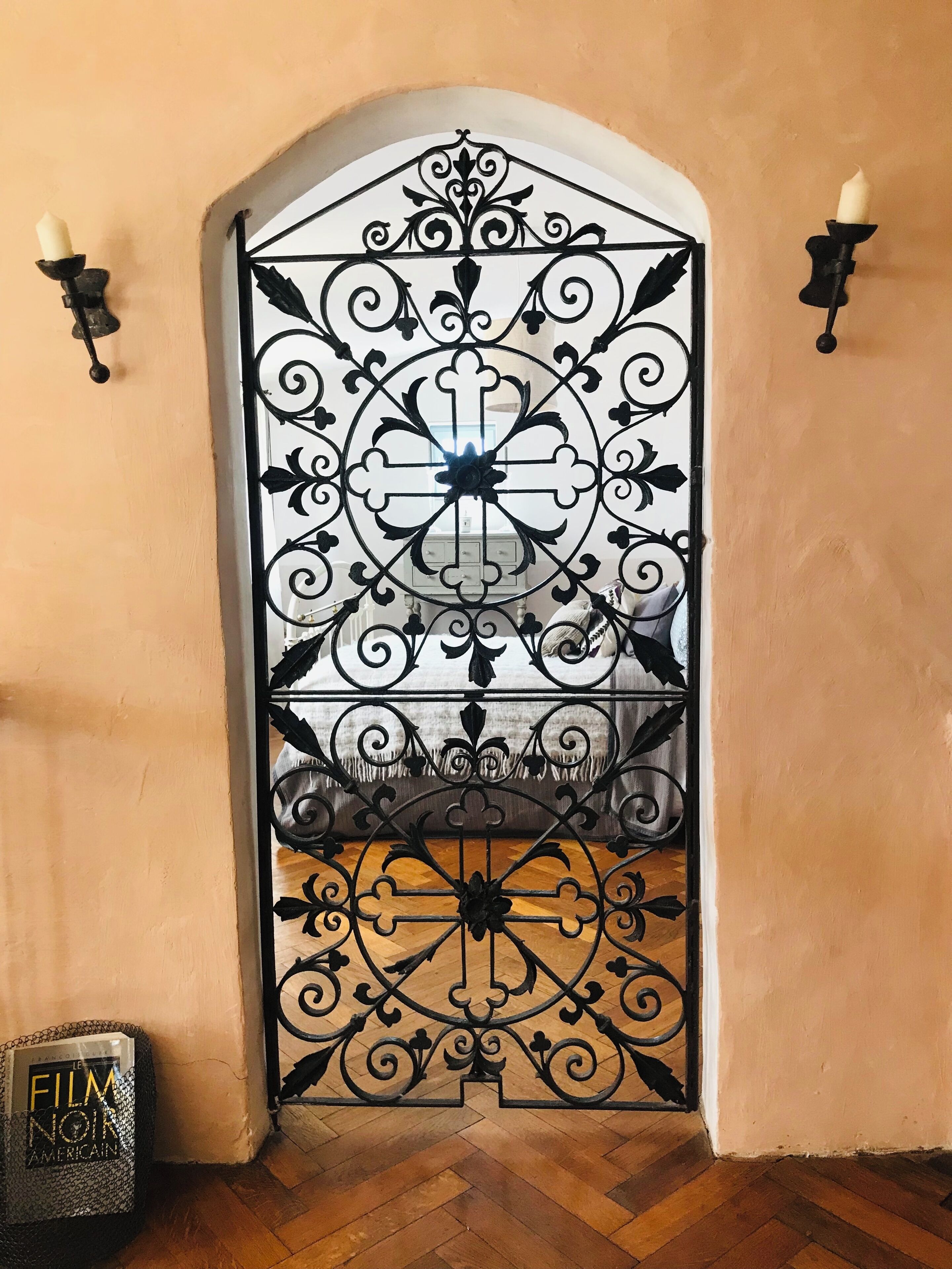 A decorative wrought iron gate with intricate designs, a white door, and a wooden floor.
