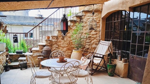 Eine Terrasse mit einem runden Tisch und Stühlen, umgeben von Steinmauern und Pflanzkübeln.