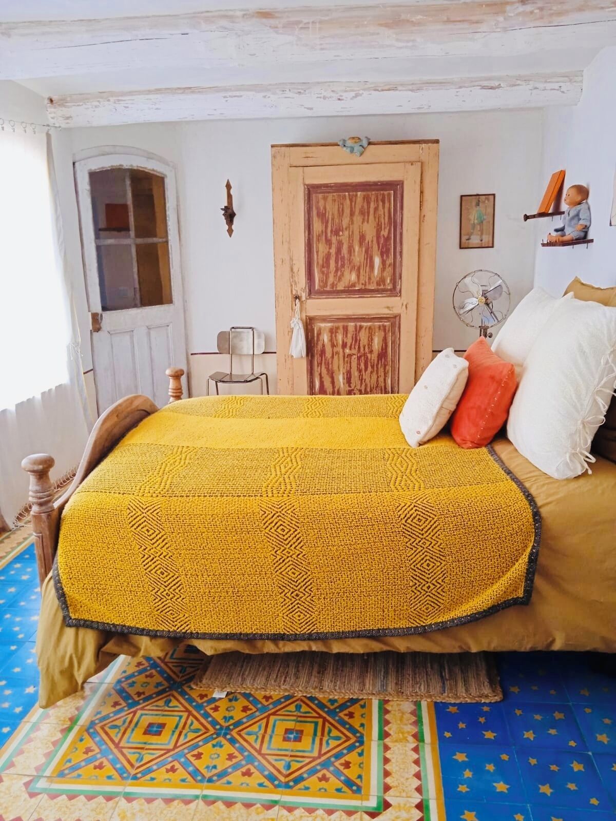 Ein Zimmer mit einem Bett, einer Holztür, einem kleinen Tisch und einem Ventilator.