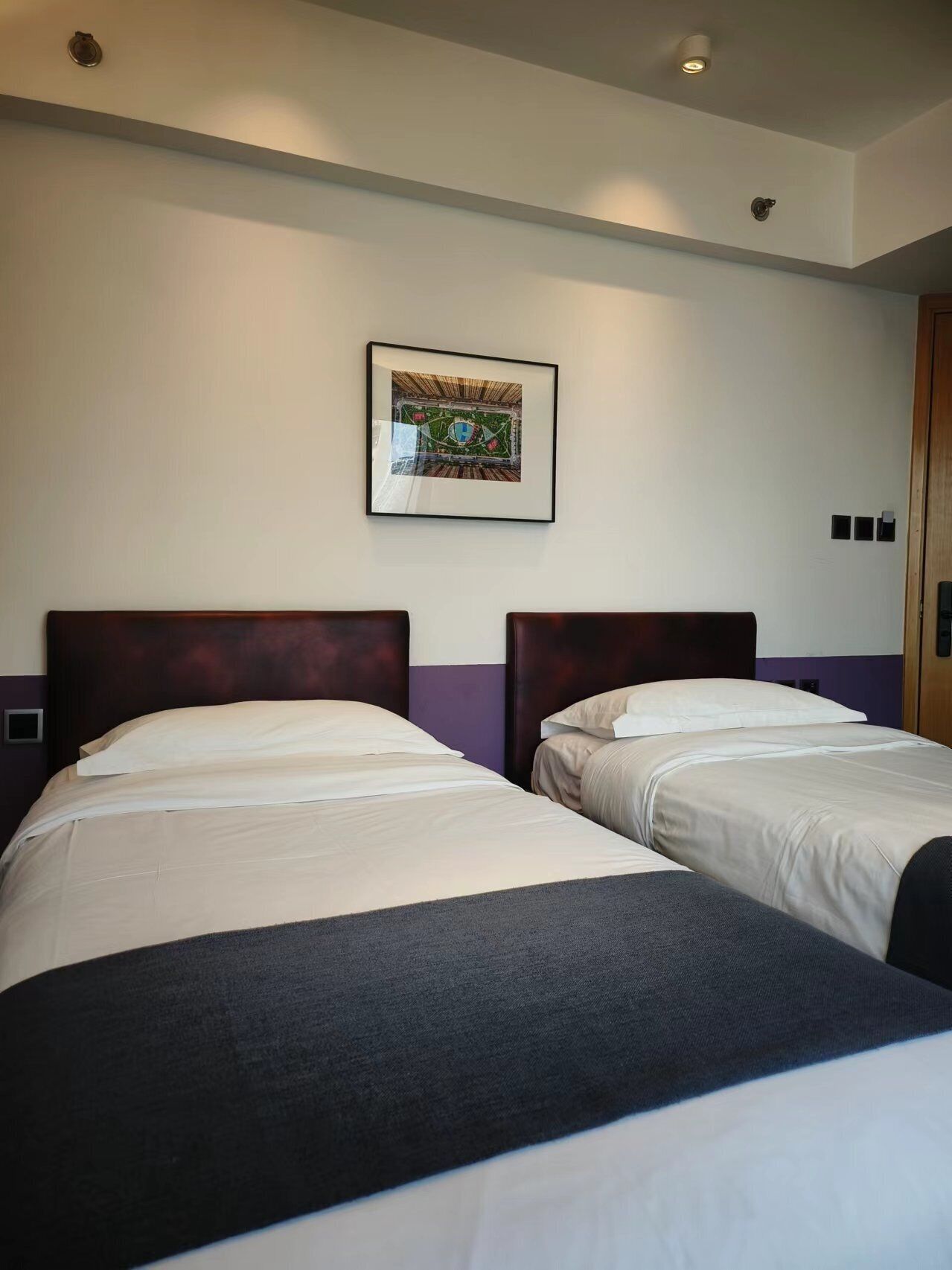 A hotel room with two beds, a framed picture on the wall, and a door to the right.