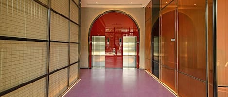 A hallway with a purple floor, a red archway, and a view of elevators in the distance.