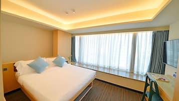 Una habitación de hotel con una cama grande, un escritorio con silla, televisión y una ventana con cortinas.
