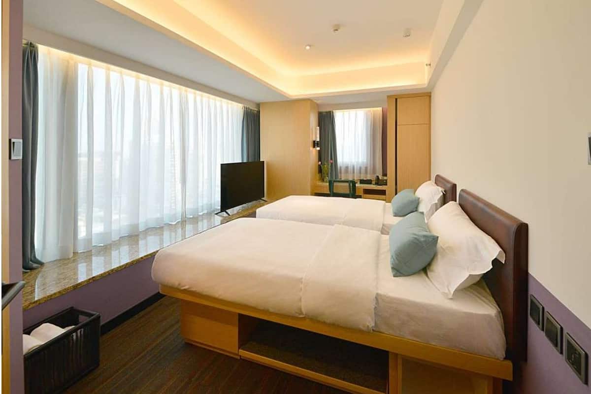 A modern hotel room with two beds, a TV, a desk, and a large window with curtains.