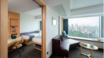 A hotel room with a bed, desk, chair, and a view of the city.