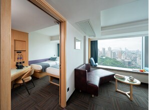 A hotel room with a bed, desk, chair, and a view of the city.