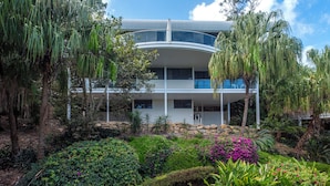 A modern building with a curved roof, surrounded by lush greenery and various plants. - Waves 2 - Ocean views with buggy (Whitsundays)