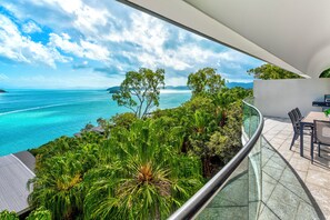 A balcony with a glass railing overlooking a turquoise sea and lush greenery. - Waves 2 - Ocean views with buggy (Whitsundays)