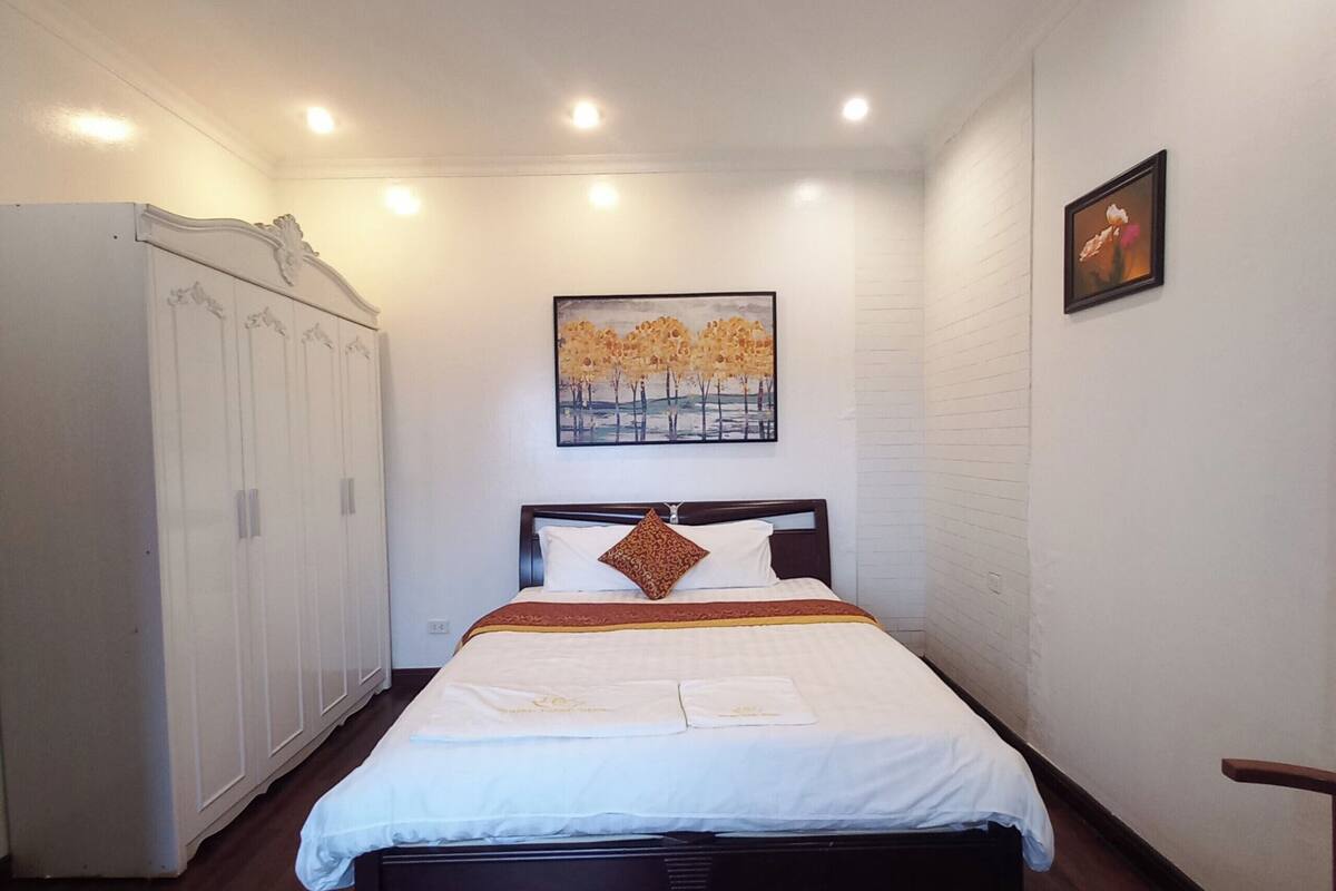 A neatly arranged bedroom with a bed, a wardrobe, and a painting on the wall.
