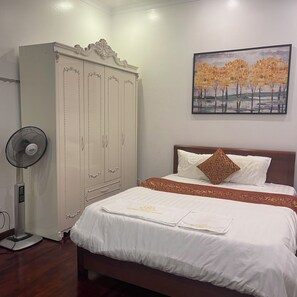A bedroom with a bed, a wardrobe, a fan, and a painting on the wall.