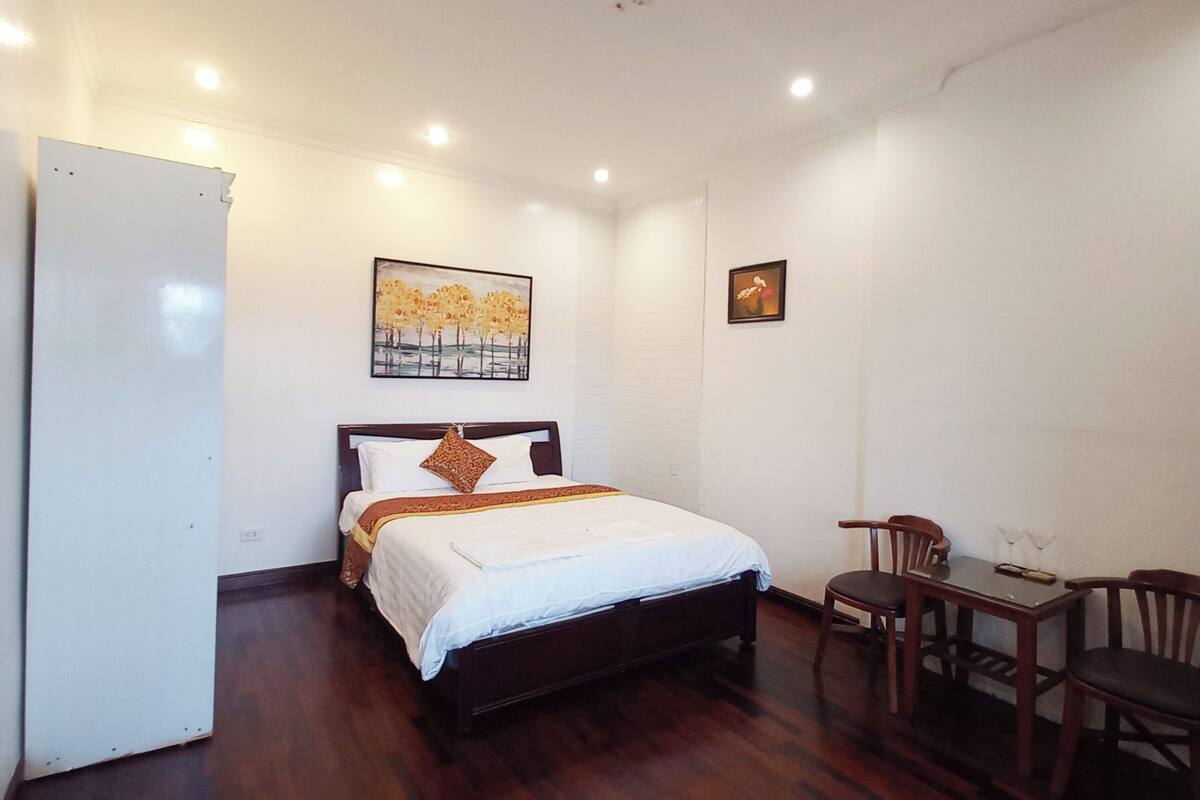 A bedroom with a wooden bed, a small table with chairs, and a refrigerator.