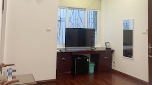 Ein Zimmer mit einem Holztisch, einem Fernseher, einer kleinen Mülltonne und einem Fenster mit Metallgitter.