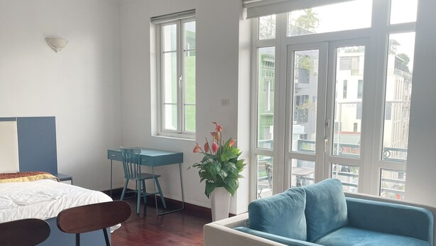 Ein modernes Zimmer mit einem Bett, einem Esstisch, einem blauen Sofa und großen Fenstern mit Blick auf Gebäude.