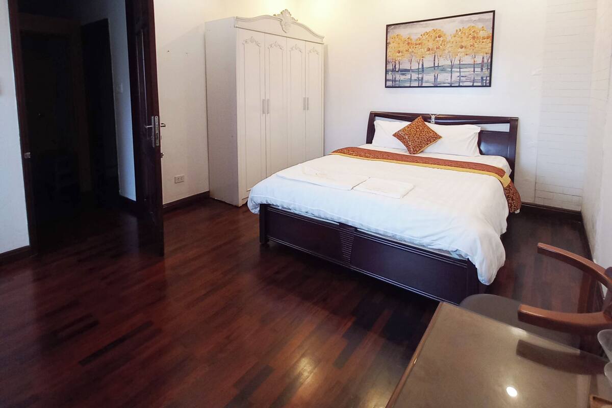 A hotel room with a bed, a wardrobe, a painting on the wall, and a table.
