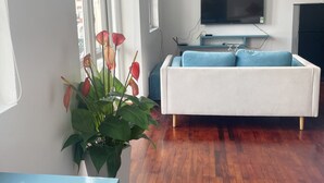Ein modernes Wohnzimmer mit einem weißen Sofa, einem flachbildfernseher an der Wand und einem Blumentopf mit roten Blüten.