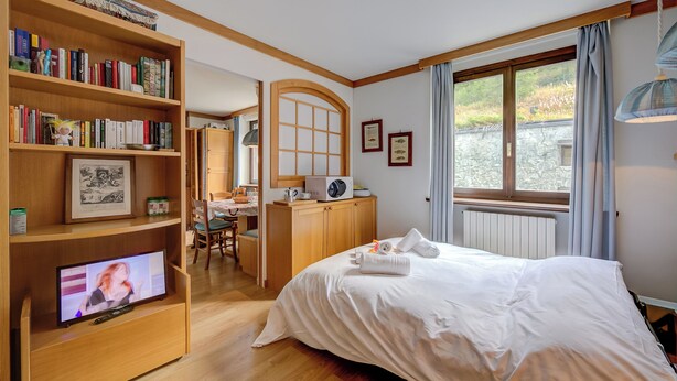 A hotel room with a bed, a TV, a bookshelf, a desk, and a window. - Appartamento Alpetta 37 Ski In - Ski Out (Sestriere)
